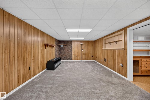 Paneled walls, brick accent wall, built-in shelving, dropped ceiling with recessed lighting, and grey carpeting - 2011 151 Avenue Nw, Edmonton, AB - Indoor