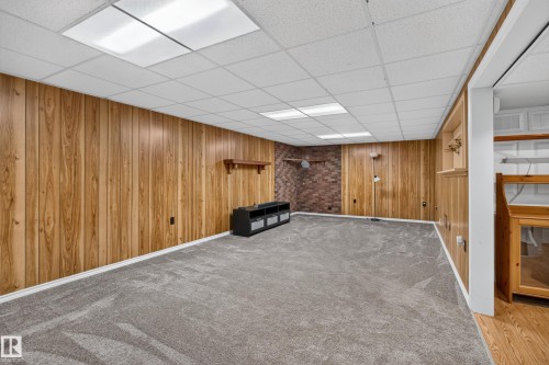 Spacious room featuring wood paneling, exposed brick accent wall, recessed lighting, and carpet flooring - 2011 151 Avenue Nw, Edmonton, AB - Indoor
