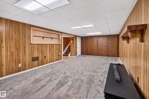 Spacious finished basement featuring warm wood-paneled walls, neutral carpeting, recessed ceiling lighting, and a staircase providing access to upper levels - 2011 151 Avenue Nw, Edmonton, AB - Indoor