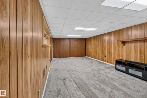 Wood paneling throughout, built-in shelving, gray carpeted flooring, drop ceiling with integrated lighting, and double bi-fold closet doors - 2011 151 Avenue Nw, Edmonton, AB - Indoor