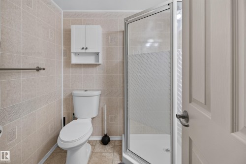 Tile flooring and walls featuring an accent band, white toilet, white wall-mounted storage cabinet, and a glass-enclosed shower with a white base - 2011 151 Avenue Nw, Edmonton, AB - Indoor Photo Showing Bathroom