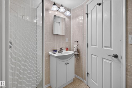 Tiled shower with patterned glass enclosure, white vanity with integrated sink, wall-mounted light fixture, and arched panel door - 2011 151 Avenue Nw, Edmonton, AB - Indoor Photo Showing Bathroom