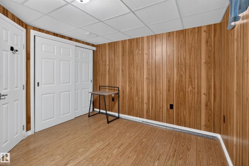Wood-finish flooring with vertical wood-paneled walls, white sliding closet doors, and a drop ceiling with recessed lighting - 2011 151 Avenue Nw, Edmonton, AB - Indoor Photo Showing Other Room