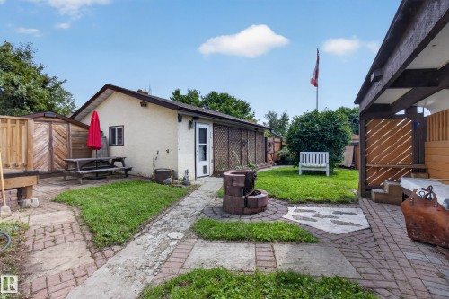 Expansive backyard featuring a brick paver pathway, a built-in brick fire pit, and an attached covered patio structure - 2011 151 Avenue Nw, Edmonton, AB - Outdoor With Deck Patio Veranda