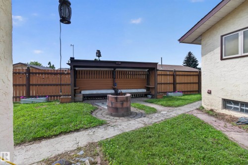 Expansive backyard retreat featuring a wood-finish privacy fence, brick paver patio with central fire pit, mature landscaping with lush lawn, and attached wooden pergola structure - 2011 151 Avenue Nw, Edmonton, AB - Outdoor