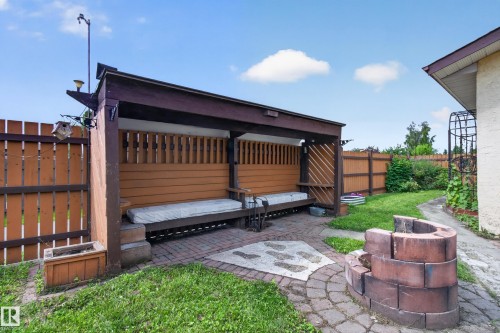 Backyard retreat featuring a custom wood-finish pergola with integrated storage, paver patio, mature landscaping, and brick fire pit—ideal for outdoor entertaining and relaxation - 2011 151 Avenue Nw, Edmonton, AB - Outdoor With Exterior