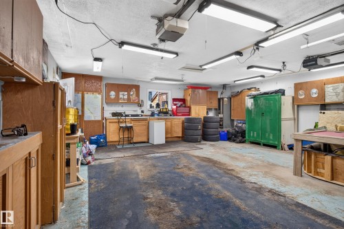 Expansive garage featuring multiple built-in wood cabinets, a workstation with a sink, overhead fluorescent lighting, and a durable concrete floor - 2011 151 Avenue Nw, Edmonton, AB - Indoor Photo Showing Garage