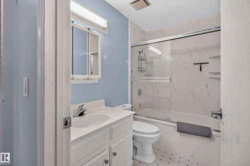Bathroom with a single vanity, an integrated sink, a built-in medicine cabinet, a toilet, and a shower-tub combination with sliding glass doors - 2011 151 Avenue Nw, Edmonton, AB - Indoor Photo Showing Bathroom