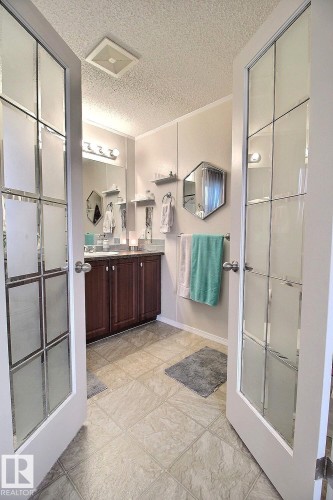 Bathroom featuring double French doors with frosted glass, a wood-finish vanity with an integrated sink, and an overhead vanity light fixture - 417 Oak Wood Crescent Northwest, Edmonton, AB - Indoor Photo Showing Other Room