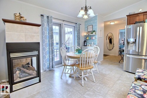 Tile-surround fireplace with a wood mantle, French doors, stainless steel refrigerator, and tiled flooring - 417 Oak Wood Crescent Northwest, Edmonton, AB - Indoor Photo Showing Dining Room With Fireplace