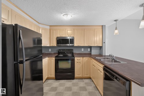 U-shaped kitchen with light wood-finish cabinetry, black appliances, a double basin sink, and pendant lighting - #205 6315 135 Av Nw, Edmonton, AB - Indoor Photo Showing Kitchen With Double Sink