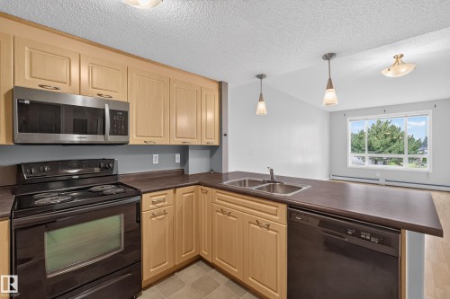 Kitchen featuring wood cabinetry, stainless steel microwave, black range, integrated dishwasher, and dual basin sink - #205 6315 135 Av Nw, Edmonton, AB - Indoor Photo Showing Kitchen With Double Sink