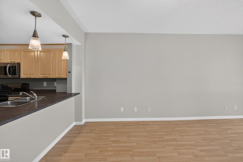 Open-concept living space featuring warm wood-finish flooring, neutral wall finishes, and abundant natural light - #205 6315 135 Av Nw, Edmonton, AB - Indoor Photo Showing Kitchen With Double Sink