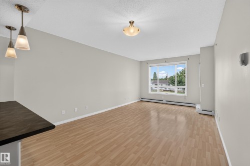 Spacious room with wood-finish flooring, large window, and suspended pendant lighting - #205 6315 135 Av Nw, Edmonton, AB - Indoor Photo Showing Other Room