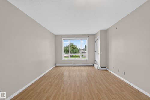 Spacious room with wood-finish flooring, a large window, a white trim package, and a white ceiling - #205 6315 135 Av Nw, Edmonton, AB - Indoor Photo Showing Other Room