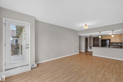 Open-concept living area featuring wood-finish flooring, a white glass-paneled door, recessed lighting, a breakfast bar, and pendant lighting - #205 6315 135 Av Nw, Edmonton, AB - Indoor Photo Showing Other Room