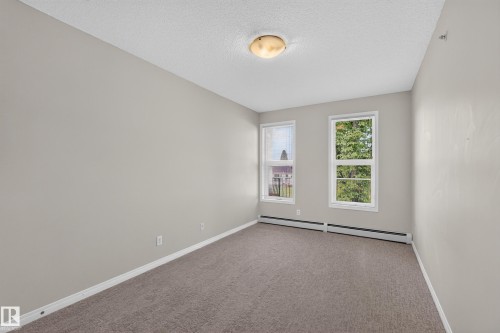 Light gray wall paint, textured ceiling, brown carpeting, two windows, and a flush mount ceiling light - #205 6315 135 Av Nw, Edmonton, AB - Indoor Photo Showing Other Room