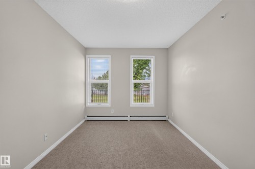 Neutral wall tones with two windows, carpeted flooring, and white trim - #205 6315 135 Av Nw, Edmonton, AB - Indoor Photo Showing Other Room