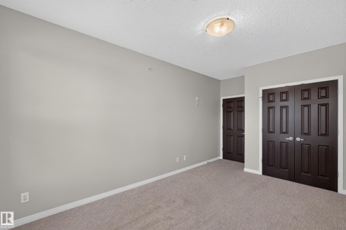 Neutral wall paint, textured ceiling, flush mount ceiling light, paneled doors, and carpet flooring - #205 6315 135 Av Nw, Edmonton, AB - Indoor Photo Showing Other Room