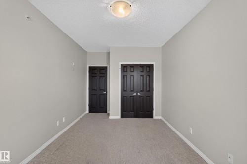 Textured ceiling with flush-mount lighting, light-toned carpet flooring, and paneled doors - #205 6315 135 Av Nw, Edmonton, AB - Indoor Photo Showing Other Room
