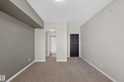 Carpet flooring, neutral wall paint, dark paneled door, flush-mount ceiling light - #205 6315 135 Av Nw, Edmonton, AB - Indoor Photo Showing Other Room