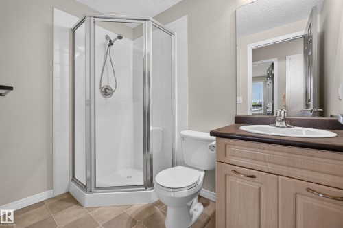 Modern bathroom featuring a corner shower enclosure with chrome framing and glass panels, a white ceramic toilet, and a wood-finish vanity with an integrated sink, black countertop, and chrome faucet - #205 6315 135 Av Nw, Edmonton, AB - Indoor Photo Showing Bathroom