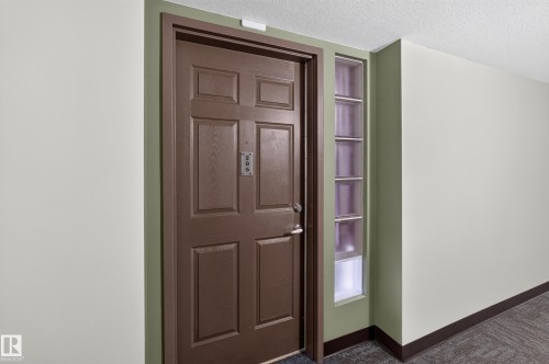 Elegant entryway showcasing a richly finished six-panel wood door with satin nickel hardware, complemented by sage-green painted trim and sidelights featuring decorative glass panes - #205 6315 135 Av Nw, Edmonton, AB - Indoor Photo Showing Other Room