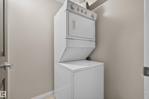 White stacked washer and dryer unit - #205 6315 135 Av Nw, Edmonton, AB - Indoor Photo Showing Laundry Room