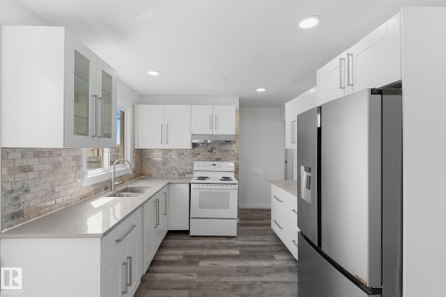 White cabinetry with brushed nickel hardware, stone-finish backsplash, wood-finish flooring, recessed lighting, and stainless steel appliances - 7823 136 Avenue Nw, Edmonton, AB - Indoor Photo Showing Kitchen With Double Sink
