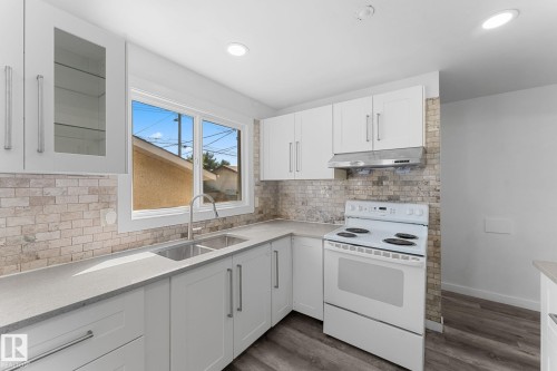 White cabinetry with brushed nickel hardware, light-toned stone backsplash, dual-basin stainless steel sink, light gray countertops, and wood-finish flooring - 7823 136 Avenue Nw, Edmonton, AB - Indoor Photo Showing Kitchen With Double Sink