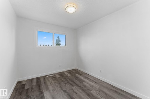 Bright interior space featuring a window with exterior scenery, white painted walls, wood-finish flooring, and an overhead light fixture - 7823 136 Avenue Nw, Edmonton, AB - Indoor Photo Showing Other Room