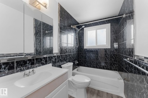 Bathroom featuring dark tiled walls, a white vanity with an integrated sink, and a white bathtub with a shower fixture - 7823 136 Avenue Nw, Edmonton, AB - Indoor Photo Showing Bathroom