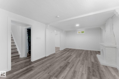 Spacious room featuring wood-finish flooring, white painted brick fireplace, and recessed lighting - 7823 136 Avenue Nw, Edmonton, AB - Indoor