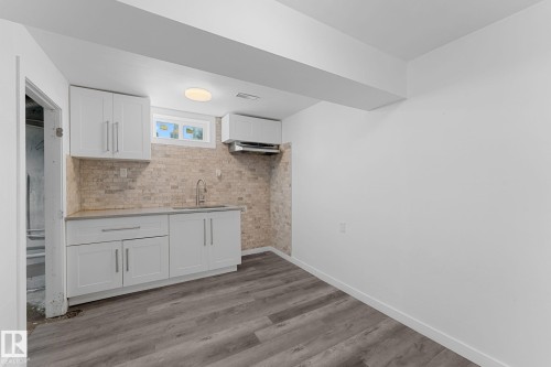 White cabinetry with brushed nickel hardware, stone-finish backsplash, undermount sink with a gooseneck faucet, light wood-finish flooring, and a flush-mount ceiling light - 7823 136 Avenue Nw, Edmonton, AB - Indoor
