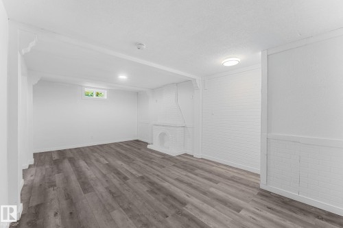 Spacious room featuring wood-finish flooring, white painted brick, and a decorative fireplace - 7823 136 Avenue Nw, Edmonton, AB - Indoor