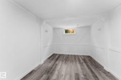 Wood-finish flooring with white baseboards, white brick-patterned wainscoting, and a single window - 
