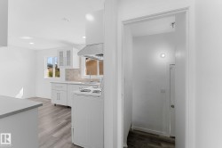 Kitchen featuring white cabinetry, light-toned countertops, a tile backsplash, and wood-finish flooring - 