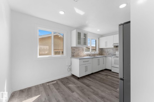 Kitchen featuring white shaker cabinetry, light-toned backsplash, gray wood-finish flooring, recessed lighting, and a stainless steel refrigerator - 7823 136 Avenue Nw, Edmonton, AB - Indoor Photo Showing Kitchen