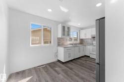Kitchen featuring white shaker cabinetry, light-toned backsplash, gray wood-finish flooring, recessed lighting, and a stainless steel refrigerator - 