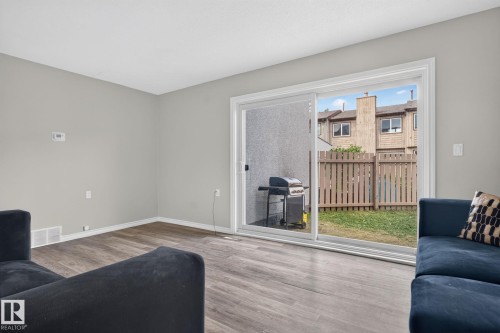 Wood-finish flooring, light gray wall paint, and a sliding glass door providing access to an outdoor area with a fenced yard - 17775 95 Street Nw, Edmonton, AB 