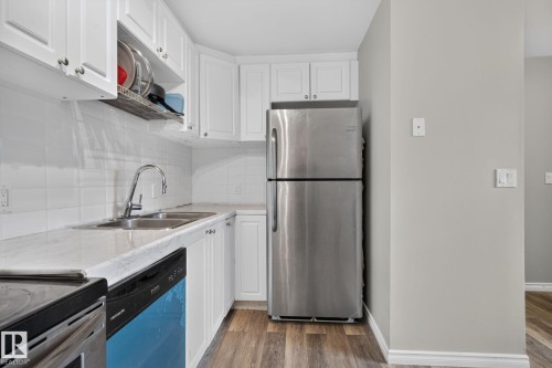 White cabinetry, white subway tile backsplash, stainless steel appliances, dual basin sink, and wood-finish flooring - 17775 95 Street Nw, Edmonton, AB 