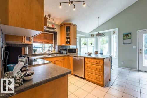 Kitchen featuring wood cabinetry, stainless steel dishwasher, tile flooring, and vaulted ceiling - 4705 43 Street, Beaumont, AB 