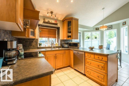 Kitchen featuring light wood cabinetry, a built-in dishwasher, tile flooring, and a vaulted ceiling - 4705 43 Street, Beaumont, AB 