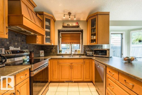 U-shaped kitchen featuring wood cabinetry, stainless steel appliances, a tiled backsplash, and recessed lighting - 4705 43 Street, Beaumont, AB 