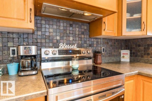 Wood cabinetry, stone tile backsplash, and stainless steel range with integrated cooktop - 4705 43 Street, Beaumont, AB 