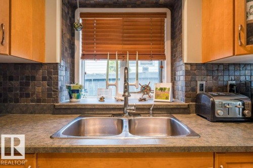 Dual basin stainless steel sink, wood-finish cabinetry, dark square tile backsplash, and solid surface countertops - 4705 43 Street, Beaumont, AB 