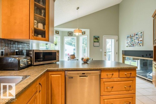 Kitchen featuring wood cabinetry, stone-finish countertops, stainless steel dishwasher, and a bay window - 4705 43 Street, Beaumont, AB 