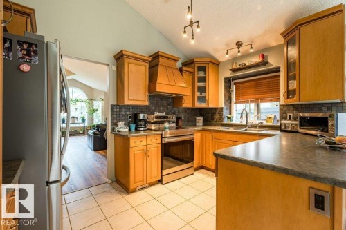 Kitchen featuring wood cabinetry, stainless steel appliances, tile flooring, and a tile backsplash - 4705 43 Street, Beaumont, AB 