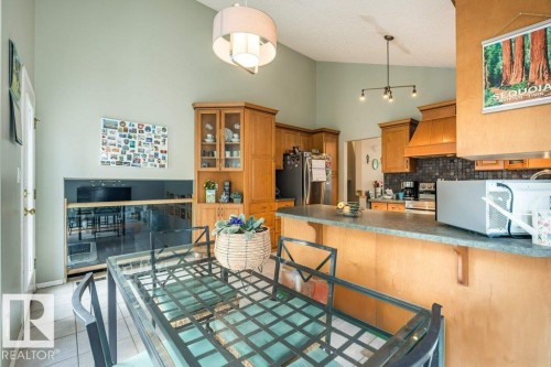Kitchen featuring vaulted ceilings, wood cabinetry, a tile backsplash, and a breakfast bar - 4705 43 Street, Beaumont, AB 