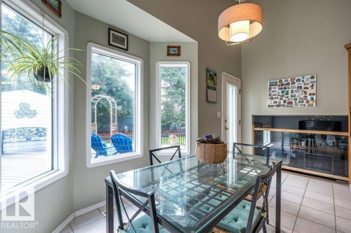 Bay window with multiple vertical pane windows, a built-in display cabinet with glass doors, a glass-top dining table, and tile flooring - 4705 43 Street, Beaumont, AB 